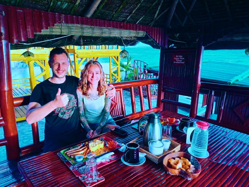 A couple at breakfast in one of the nipa huts, the sea behind them